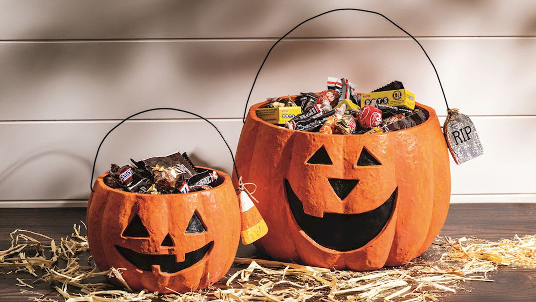 Two Halloween candy buckets with carved pumpkin faces on a wooden surface.